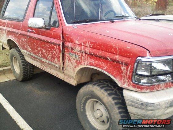 Red 1992 Ford Bronco covered in mud, front passenger side view