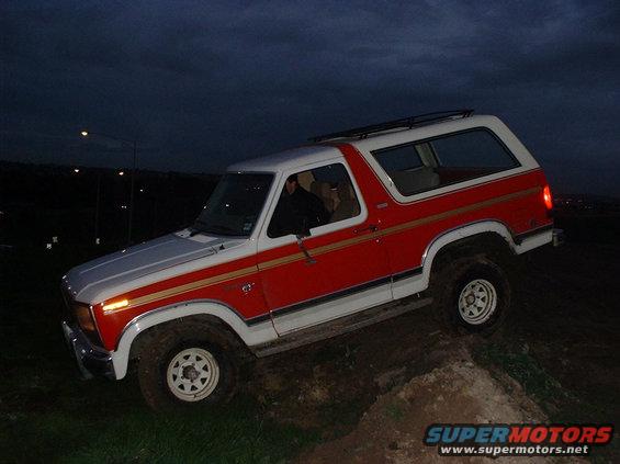 1981 Ford Bronco with red and white paint, driving off-road at dusk