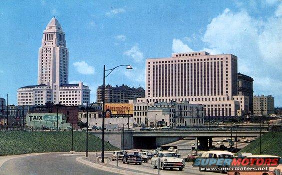 Los Angeles City Hall and other downtown buildings under a blue sky with clouds, traffic on a highway below