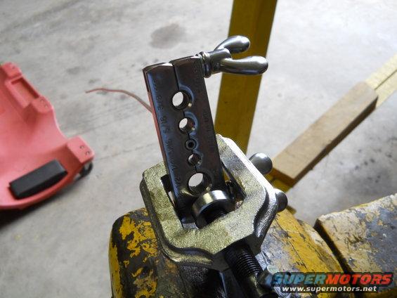 Flaring tool clamped in a vise on a workbench, with a red creeper in the background
