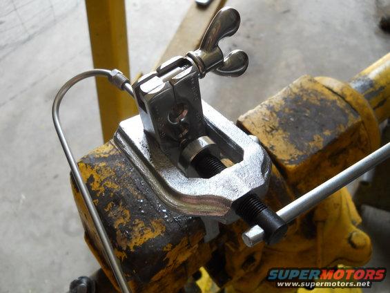 Flaring tool with a metal tube attached, clamped in a yellow vise