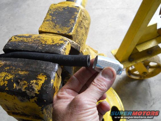 Hand holding a silver fitting near a black hose clamped in a yellow vise with "Made in USA" visible on the hose