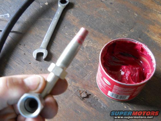 Grease gun fitting with red grease, wrench, and can of red grease
