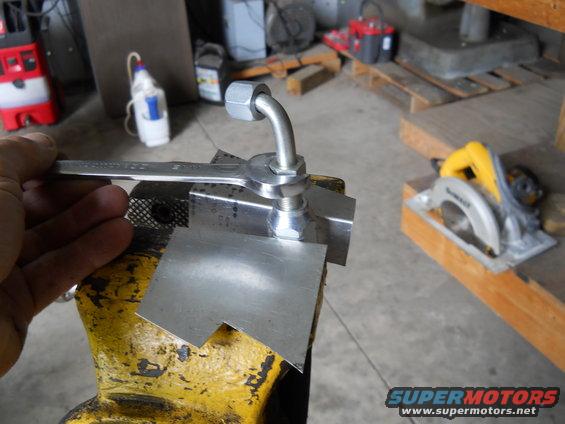 wrench tightening a metal fitting held in a vise, with a circular saw in the background