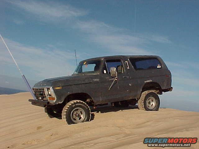Dark gray 1979 Ford Bronco parked on a sand dune under a blue sky