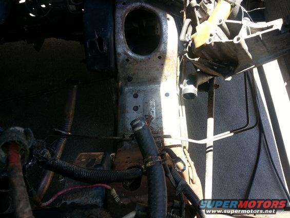 Engine bay with hoses, wires, and metal frame. Some rust visible