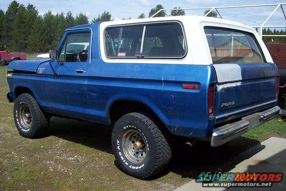 Blue and white Ford Bronco with aftermarket wheels and tires, viewed from the rear three-quarter angle