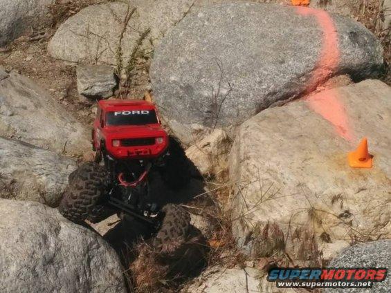 Red RC rock crawler with 'FORD' text on windshield, navigating rocky terrain