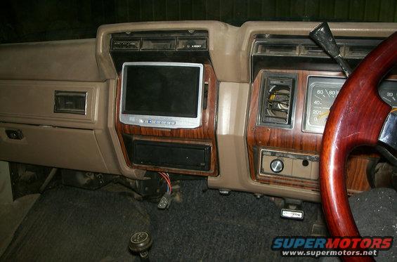 Dashboard with wood grain trim, aftermarket screen, and gauges. Steering wheel is wood