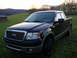 2007 Ford F-150 - A black Ford F-150 pickup truck is parked in a grassy field with hills in the background during sunset.