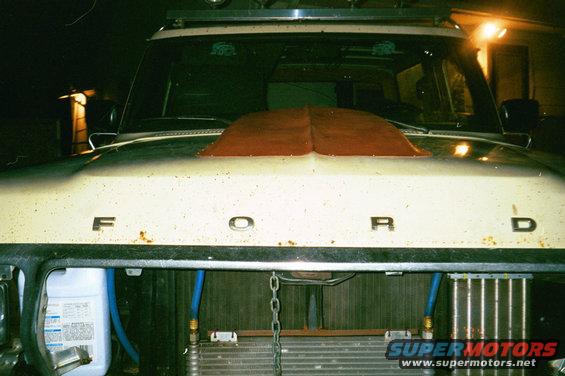 Front of a white Ford truck with a red hood scoop and visible engine components