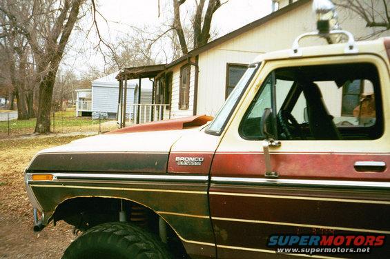 Side view of a two-tone red and tan 1979 Ford Bronco with a hood scoop and off-road tires