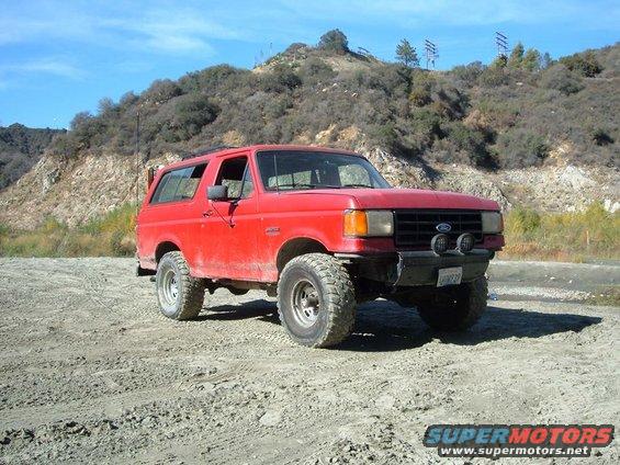 Red 1988 Ford Bronco parked on a dirt road with hills in the background