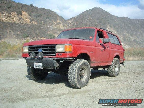 Red Ford Bronco with off-road tires parked on dirt road, mountains in background