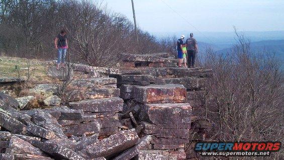 People stand on a rocky cliff edge with a valley in the background