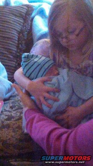 Two people holding a baby wrapped in a blue blanket and wearing a striped hat