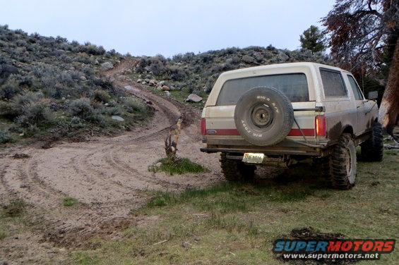 Rear view of a 1989 Ford Bronco with a spare tire on the back, parked on a muddy dirt road