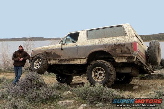 Man leaning on muddy Ford Bronco parked by a lake
