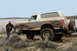 1989 Ford Bronco - A man poses with a mud-covered Ford Bronco near a body of water.