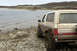 1989 Ford Bronco - A muddy 1989 Ford Bronco is parked on a rocky shore next to a body of water.
