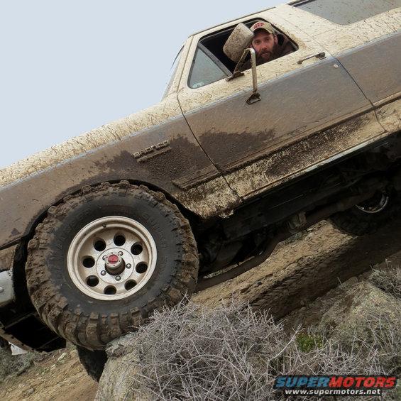 Mud-covered 1987 Ford Bronco climbing a rocky incline, driver visible