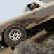 1989 Ford Bronco - A muddy 1987 Ford Bronco navigates a challenging off-road terrain with a driver at the wheel.