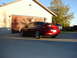 1993 Mazda MX-3 - A red 1993 Mazda MX-3 coupe is parked in front of a garage with a wooden door.
