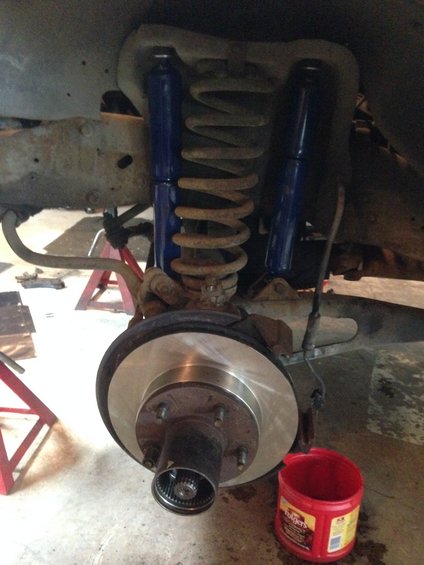 close-up of a vehicle's front brake rotor and suspension with blue shocks