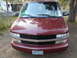 2000 Chevrolet Astro - The front of a maroon Chevrolet Astro van is shown parked outdoors with trees and a trailer in the background.