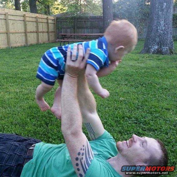 Man lying on grass holding a baby in the air