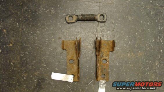 Two rusty metal brackets and a connecting rod with rubber bushing on a textured floor