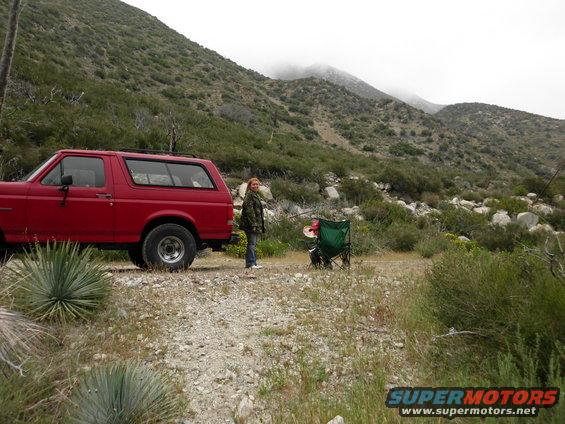 1988 Ford Bronco parked on a dirt road in a mountainous area. A person stands next to the vehicle