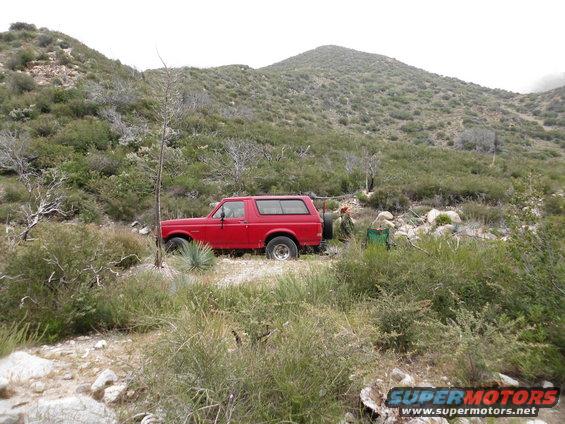 Red SUV parked on a dirt path with scrub brush and hills in the background