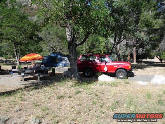 Red SUV parked near a tent and picnic table at a campsite