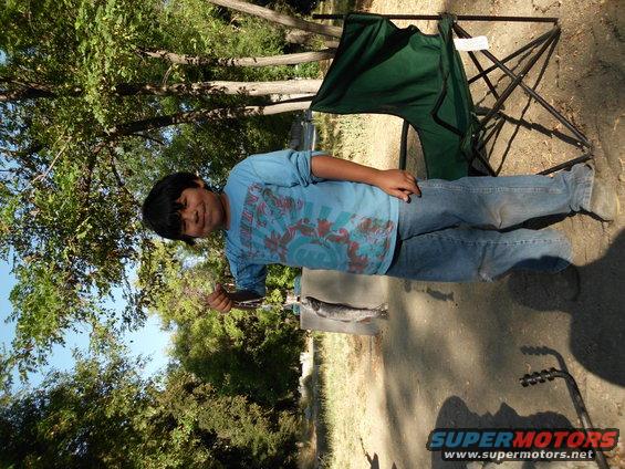 Boy holds a freshly caught fish near a green camping chair outdoors