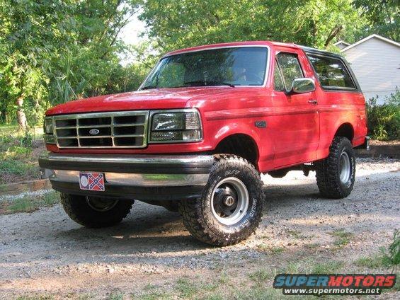 Red 1992 Ford Bronco parked on a gravel driveway with trees in the background