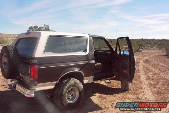 1992 Ford Bronco with spare tire on rear, doors open, parked on dirt road in desert landscape