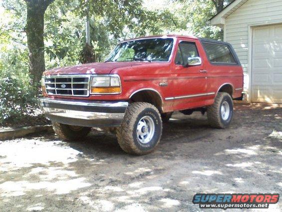 Red 1992 Ford Bronco parked in a dirt driveway next to a garage