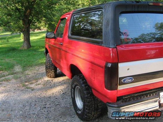 Red Ford Bronco, rear quarter view, lifted suspension, aftermarket wheels, black soft top