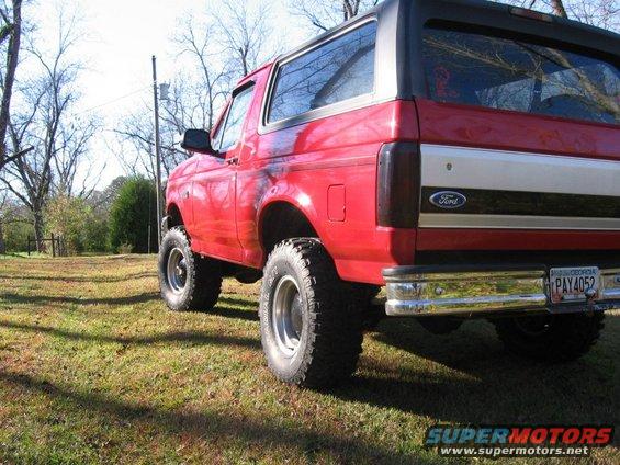 Red 1992 Ford Bronco, lifted, with aftermarket wheels, viewed from the rear three-quarter angle