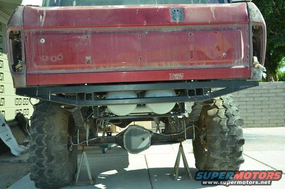 rear of red pickup truck with large off-road tires, custom bumper, and dual propane tanks underneath