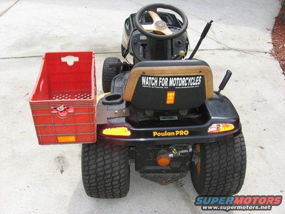 Riding mower with red milk crate attached to the back. Has 'Poulan PRO' on the rear