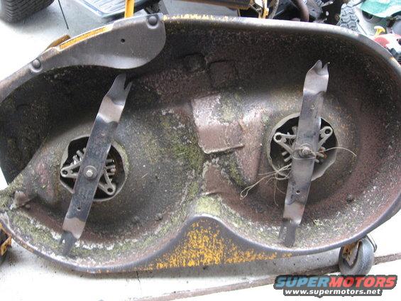 Underside of a mower deck with two blades and grass clippings