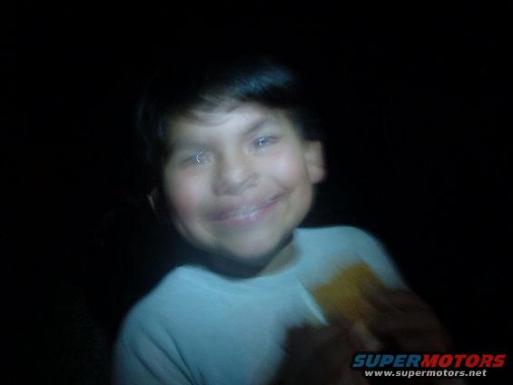 Child in a white shirt, smiling, with a dark background. Text 'SUPERMOTORS' is visible