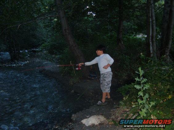 Boy fishing by a stream with Supermotors logo visible