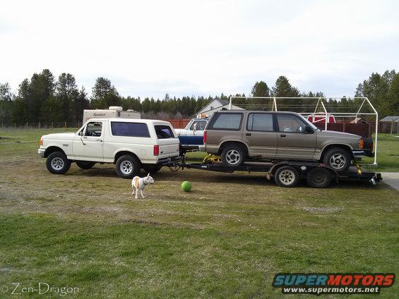 White 1990 Ford Bronco towing a brown Ford Explorer on a trailer
