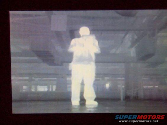 Thermal image of a person standing indoors, with "SUPERMOTORS" text at the bottom
