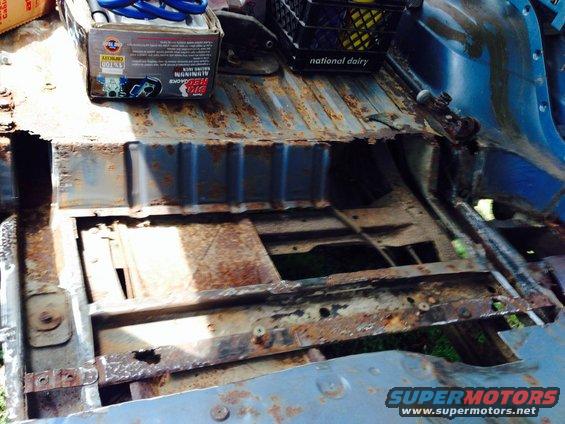 Rusted floor pan of a vehicle interior with a box of red jacks and a national dairy crate on top