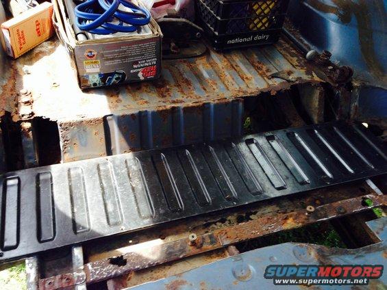 Interior cargo area with extensive rust and a black metal floor panel