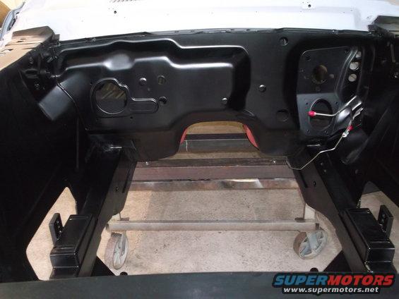Blackened engine bay of a car on a stand, showing firewall and inner fenders